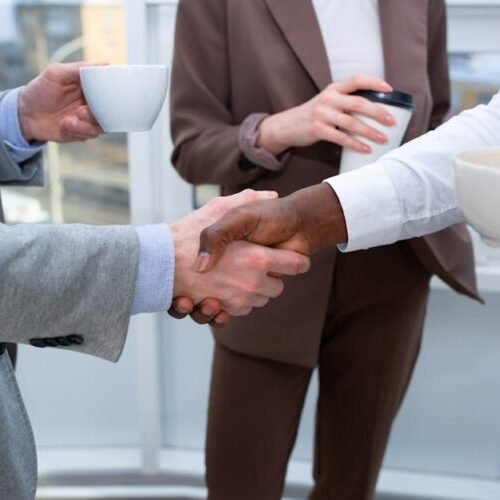 A professional handshake between colleagues holding coffee cups, symbolizing collaboration.